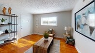 Located at 755 Anson St in Winston-Salem, NC, this single-floor home offers a practical and comfortable layout with warm, inviting interiors throughout. The living area greets visitors with rich hardwood flooring, a textured ceiling, neutral gray walls, and a front-facing window that draws in generous natural light. A rustic wood coffee table anchors the space, complemented by eclectic accent furnishings that add character.

The kitchen features white cabinetry, light countertops, and tile flooring. Black appliances — including a refrigerator, electric range, and dishwasher — provide a clean contrast to the bright cabinetry, while a window above the sink allows natural light to filter in. An in-unit washer is also conveniently located within the kitchen area.

The home includes multiple bedrooms, each finished with the same warm hardwood flooring and neutral tones. Windows in each room invite natural light and outdoor views. One bedroom features a sliding-door closet and an accent wall with exposed brick-style detailing, adding a distinctive design touch.

The bathroom is tastefully finished with a dark-framed vanity mirror, a white sink with brushed nickel fixtures, tile surround, and a shower-tub combination. Overall, the home presents a cohesive, understated aesthetic with functional, well-maintained spaces throughout.