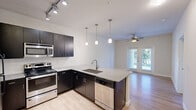 Located at 9301 Old Bee Caves Rd in Austin, TX, this one-bedroom, one-bathroom residence offers a well-designed layout across a single floor. The open-concept kitchen is a standout feature, equipped with dark espresso cabinetry, granite countertops, stainless steel appliances including a refrigerator, electric range, microwave, and dishwasher, and a central peninsula with an undermount sink. Track lighting and elegant pendant lights illuminate the kitchen, which flows seamlessly into the living area. The living space features light wood-style flooring, a ceiling fan, and French doors that invite natural light and provide access to an outdoor area with views of surrounding greenery. The bedroom is carpeted for comfort, features a ceiling fan, and includes a large window with an outdoor view, offering a bright and peaceful retreat. A dedicated closet provides convenient storage. The bathroom is finished with wood-style flooring, dark cabinetry with a granite-topped vanity, and a full tub-shower combination with white tile surround. Clean white walls and consistent modern finishes throughout create a cohesive and contemporary living environment.