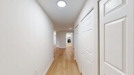 Located at 5029 Columbia Rd in Columbia, MD, this 2-bedroom, 2-bathroom single-floor home offers a clean, modern aesthetic throughout. Light wood-tone flooring flows across the main living areas, complementing a neutral color palette of crisp whites and soft grays that lend a bright, airy feel to every room.

The spacious living area serves as the heart of the home, featuring a sleek wall-mounted electric fireplace and a large sliding glass door that floods the space with natural light and provides access to an outdoor area with wooded views. The kitchen is well-equipped with white shaker-style cabinetry, stainless steel appliances including a range, refrigerator, and dishwasher, white countertops with a tile backsplash, and a sink with a sliding glass door nearby for additional natural light.

Both bedrooms are carpeted for warmth and comfort. The primary bedroom is generously sized, featuring a bay window with lush outdoor views and a closet. The second bedroom also includes a window and a closet, offering ample storage. A connecting hallway provides convenient access to both bedrooms and bathrooms.

Each bathroom is finished in white with a vanity, toilet, and a tub-shower combination with a curtain rod. The overall design of this home is clean, cohesive, and move-in ready.