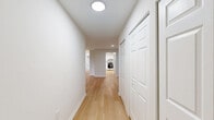 Located at 5029 Columbia Rd in Columbia, MD, this 2-bedroom, 2-bathroom single-floor home offers a clean, modern aesthetic throughout. Light wood-tone flooring flows across the main living areas, complementing a neutral color palette of crisp whites and soft grays that lend a bright, airy feel to every room.

The spacious living area serves as the heart of the home, featuring a sleek wall-mounted electric fireplace and a large sliding glass door that floods the space with natural light and provides access to an outdoor area with wooded views. The kitchen is well-equipped with white shaker-style cabinetry, stainless steel appliances including a range, refrigerator, and dishwasher, white countertops with a tile backsplash, and a sink with a sliding glass door nearby for additional natural light.

Both bedrooms are carpeted for warmth and comfort. The primary bedroom is generously sized, featuring a bay window with lush outdoor views and a closet. The second bedroom also includes a window and a closet, offering ample storage. A connecting hallway provides convenient access to both bedrooms and bathrooms.

Each bathroom is finished in white with a vanity, toilet, and a tub-shower combination with a curtain rod. The overall design of this home is clean, cohesive, and move-in ready.