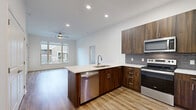 Located in Olathe, Kansas, this single-story 2-bedroom, 2-bathroom residence offers a thoughtfully designed layout with contemporary finishes throughout. The open-concept living, dining, and kitchen area serves as the heart of the home, filled with natural light from large picture windows that frame views of the surrounding neighborhood. Warm wood-look flooring extends through the main living spaces, complemented by ceiling fans for year-round comfort.

The kitchen is a standout feature, boasting rich dark wood cabinetry, a peninsula island with a white quartz countertop and undermount sink, a tile backsplash, and a full suite of stainless steel appliances including a refrigerator, range, microwave, and dishwasher. Recessed lighting adds a clean, modern touch overhead.

Both bedrooms are carpeted and bathed in natural light, with the spacious primary bedroom offering direct access to its own en-suite bathroom. The primary bath includes a walk-in tiled shower with glass doors, a wood-tone vanity with quartz countertop, and wood-look flooring. The second bathroom features a soaking tub with tiled surround. Three closets provide generous storage, including a walk-in closet with built-in shelving and hanging rods. A private patio, laundry area, and utility room round out this well-appointed residence.