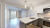 Located at 15 Cooper's Town Road in Winnipeg, this well-appointed one-bedroom unit offers a thoughtfully designed open-concept layout that maximizes its efficient footprint. The combined kitchen and living area serves as the heart of the home, showcasing a sleek peninsula island with a crisp white quartz countertop, double stainless steel sink, and pendant lighting overhead. The kitchen is equipped with a full suite of stainless steel appliances, including a refrigerator, stove, and built-in microwave, complemented by white gloss upper cabinetry and a contemporary tile backsplash. Light hardwood-style flooring runs throughout the main living space, enhancing the bright, airy atmosphere created by recessed ceiling lights. A sliding glass door in the living area opens to a private balcony, inviting natural light and outdoor views into the space. The bedroom offers plush carpeting, a bold accent wall, a large window for additional natural light, and a sliding-door closet with built-in shelving. A stylish barn-style sliding door provides an architectural accent near the entryway. The unit combines modern design elements with functional details to create a clean, contemporary living environment.