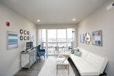 This single-floor unit blends industrial design elements with comfortable living spaces. The kitchen is a standout feature, showcasing warm wood cabinetry, stainless steel appliances including a refrigerator, electric range, and microwave, all complemented by a white countertop island with bar seating. Exposed ductwork runs along the ceiling, adding an urban, loft-inspired character, while pendant lighting reinforces the industrial aesthetic. The open living area flows seamlessly from the kitchen and is filled with natural light through large sliding glass doors that lead to a private balcony, offering open outdoor views.

The unit includes two bedrooms, each equipped with ceiling fans and carpeted flooring. One bedroom features a large window with an exterior view, while the other benefits from a built-in open closet system. Both bathrooms are finished with wood-toned cabinetry, white countertops, and wood-look flooring, providing a clean and cohesive look. A dedicated laundry area houses a full-sized washer and dryer, adding everyday convenience. Throughout the unit, neutral wall tones create a calm, versatile backdrop.