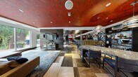 Located at 101 10th St E in Saint Paul, Minnesota, this single-floor amenity space is a masterclass in bold, eclectic interior design. The most immediately striking feature is the richly embossed, deep red patterned ceiling that spans much of the space, creating a dramatic overhead focal point that ties the various zones together with cohesive visual energy.

The open-plan layout encompasses a fully equipped gourmet kitchen and bar area anchored by an expansive granite-topped island with bar seating. Dark wood cabinetry, a built-in wine cooler, and a mirrored, diamond-patterned ceiling above the bar add layers of sophistication. Geometric pendant lighting and metallic accents further enhance this area's upscale character.

A dedicated lounge zone features a large sectional sofa, plush area rugs, and floor-to-ceiling windows that flood the space with natural light and provide direct access to an outdoor patio. Adjacent to this is a game area complete with a full-length shuffleboard table, horizontal wood-paneled walls, and globe pendant lights.

A private dining alcove offers a long banquette upholstered in bold red fabric, paired with a reclaimed wood table and surrounded by textured, sculptural white walls. Throughout the space, the multi-toned geometric tile and hardwood flooring adds yet another layer of artistic detail, making this an exceptionally well-appointed and visually dynamic gathering space.