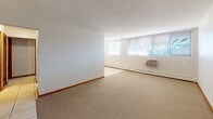 Located at 6116 Lyndale Ave S in the Fulton neighborhood of Minneapolis, Minnesota, this single-floor unit offers a clean, straightforward layout designed for comfortable everyday living. The open living area is generously sized, featuring neutral-toned carpet, white walls with warm wood baseboard trim, and large windows fitted with horizontal blinds that allow abundant natural light to fill the space. A wall-mounted air conditioning unit and baseboard heating ensure year-round climate comfort. The kitchen is practical and well-appointed, offering rich dark wood cabinetry, light-toned countertops, and a deep double stainless steel sink. Light tile flooring in the kitchen and entry areas provides a functional contrast to the carpeted living and sleeping spaces. The bedroom is comfortably sized, featuring carpet, baseboard heating, and windows that bring in natural light, along with a ceiling fan for added ventilation. A second room, also carpeted, offers additional flexible space. The full bathroom includes a tub-shower combination with white tile surround, a white vanity, a toilet, a warm wood door, and classic mosaic tile flooring, creating a tidy and functional space. Overall, the unit presents a neutral, move-in-ready environment well-suited for residential living in south Minneapolis.