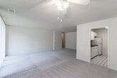 This single-floor unit offers a practical and straightforward layout connecting a generously sized living area, a dedicated kitchen, multiple carpeted rooms, and a full bathroom. The living area is broad and open, featuring neutral-toned wall-to-wall carpeting, a textured ceiling, and a ceiling fan with a light fixture. Large sliding glass doors dressed with vertical blinds span much of one wall, flooding the space with natural light and offering views of surrounding greenery. A secondary living or dining area adjacent to the main space shares the same carpet and ceiling fan details, maintaining a cohesive feel throughout.

The galley-style kitchen is efficiently arranged, with white cabinetry lining both sides from floor to ceiling, providing ample storage. Dark countertops contrast cleanly with the white surfaces, and appliances include a gas range, built-in microwave, refrigerator, and dishwasher. The kitchen floor features a classic black-and-white tile pattern that also carries into the bathroom.

The bedrooms are carpeted and well-lit, with windows fitted with vertical blinds offering natural light and outdoor views. Each room provides a calm, neutral backdrop. The bathroom is clean and functional, featuring a tub-shower combination with white tile surround, a single-sink vanity, and the same black-and-white diamond tile flooring seen in the kitchen.