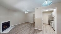 This single-floor residence presents a cohesive, neutral design highlighted by warm wood-look flooring that flows continuously throughout the living areas, kitchen, bedroom, and bathroom. The open layout connects a spacious living room to the kitchen, creating a practical and inviting flow. The living room serves as the centerpiece of the unit, featuring a white-mantled fireplace with a tiled surround, a ceiling fan with integrated lighting, and a window fitted with horizontal blinds that allows natural light to fill the room.

Adjacent to the living area, the kitchen is outfitted with stainless steel appliances, including a refrigerator and electric range, complemented by white cabinetry, a ventilation hood, and light countertops. A pass-through opening connects the kitchen to the main living space, enhancing the sense of openness.

The bedroom offers a ceiling fan, a closet with double bi-fold doors, and a calm, neutral color palette. The bathroom features a white vanity with storage, a large mirror, wood-look flooring consistent with the rest of the unit, and brushed nickel hardware accents. Textured ceilings and clean white trim throughout contribute to the overall polished appearance of the space.