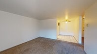 This single-story unit is thoughtfully laid out across several distinct areas, offering a functional and straightforward floor plan. The living area is generously sized, featuring wall-to-wall carpeting that extends throughout the main living spaces and bedrooms, providing a comfortable underfoot feel. A ceiling fan with a light fixture overhead serves the main living area, while a sliding glass door opens to an outdoor patio, allowing natural light to fill the space and providing direct exterior access. A built-in wall HVAC unit ensures efficient climate control throughout the living areas.

The kitchen is outfitted with dark cabinetry featuring decorative paneling and gold-toned hardware, offering ample upper and lower storage. Light tile flooring, a double-basin sink, a dishwasher, a refrigerator, and a range complete the kitchen's functional setup. The tiled entry area flows naturally from the kitchen toward the main living space.

The bedrooms are carpeted and well-proportioned, each featuring neutral white walls and natural light from windows with vertical blinds. At least one bedroom includes a closet with a bifold door. The bathroom includes a tub-shower combination, a vanity with a speckled countertop, dark cabinetry below, a mirror, and tile flooring, creating a clean and practical space.