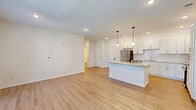 Located at 14744 Malachi Rd in Noblesville, Indiana, this well-designed one-bedroom, one-bathroom residence offers a thoughtful layout across a single floor. The open-concept kitchen and living area serves as the heart of the home, featuring light-toned luxury vinyl plank flooring, crisp white shaker cabinetry, a subway tile backsplash, and a full suite of stainless steel appliances including a refrigerator, range, microwave, and dishwasher. A central kitchen island with a striking granite countertop provides additional prep space and seating, while stylish pendant lights hang overhead, adding a modern touch. Recessed lighting and windows allow natural light to fill the shared living space. The bedroom is a comfortable and private retreat, finished with plush wall-to-wall carpet, a ceiling fan, and a window with blinds. An adjacent walk-in closet offers built-in wire shelving for organized storage. The bathroom is clean and functional, featuring light wood-look flooring, a walk-in shower with grab bars, and a vanity with a marble-style countertop. A hallway connects the main living areas, completing this efficient and attractively finished single-story residence.