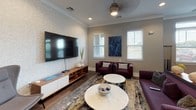 Located at 1500 Water Lily Dr in Simpsonville, South Carolina, this single-floor community clubhouse offers a well-appointed gathering space designed for both productivity and recreation. The interior is finished with rich hardwood flooring, neutral-toned walls with textured wallcoverings, and crown molding that lends a polished, contemporary aesthetic throughout.

The business center features a long, shared workstation accommodating multiple users, equipped with desktop computers and ergonomic task chairs. Elegant pendant lighting hangs above the desk area, while framed abstract artwork adorns the textured accent wall, creating a professional yet welcoming atmosphere.

Adjacent to the workspace is a comfortable lounge area furnished with deep burgundy seating, marble-topped coffee tables, and a patterned area rug. A large wall-mounted flat-screen television serves as a focal point, complemented by a ceiling fan and multiple windows that allow natural light to fill the space.

The billiards room is a standout feature, centered around a full-size pool table with a vibrant blue felt surface beneath a striking sputnik-style chandelier set within a tray ceiling. Windows along the perimeter provide views of the surrounding community. Small bistro tables and chairs offer additional seating, making this an ideal social hub. A wet bar or kitchenette area with dark cabinetry completes the space.