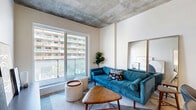Located at 300 Avenue de l'Équinoxe in Brossard, this well-designed one-bedroom, one-bathroom unit offers a thoughtful layout across a single floor. The open-concept living and dining area is defined by striking exposed concrete ceilings and light hardwood flooring, creating an industrial-modern aesthetic. A pendant light anchors the dining space, which flows naturally into a bright living area with large windows that invite natural light and urban views.

The kitchen is sleek and functional, featuring floor-to-ceiling cabinetry in a muted grey tone, stainless steel appliances including a full-size refrigerator and range, and a generous island with a white quartz countertop and undermount sink — ideal for both cooking and casual dining.

The bedroom is a calm retreat, benefiting from wide windows with exterior views, warm lighting, and exposed concrete ceiling details consistent with the unit's overall design language. Light hardwood floors continue throughout.

The bathroom is finished in a clean, contemporary style with large-format tile flooring, a floating vanity with an under-mount sink, a backlit mirror, and a combined shower-bathtub with elegant tiling. A dedicated laundry area with a stacked washer and dryer unit and built-in shelving adds everyday convenience to this efficiently designed home.