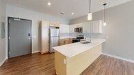 This single-story residence showcases a thoughtfully designed open-concept layout with consistent wood-look flooring flowing throughout the living areas. The kitchen serves as a central highlight, featuring a combination of light natural wood and white shaker-style cabinetry, white quartz countertops, and a full suite of stainless steel appliances including a refrigerator, electric range, microwave, and dishwasher. A peninsula island with an integrated sink and pendant lighting above extends the workspace while connecting seamlessly to the living area. A sliding glass door fitted with vertical blinds brings natural light into the living space and provides outdoor access.

The bedrooms are finished with the same wood-look flooring and neutral gray walls, each equipped with ceiling fans. One bedroom features a walk-in closet, while another benefits from a large window with horizontal blinds. The bathroom is cleanly appointed with a walk-in shower, a light wood vanity with a white countertop, and matching wood-look tile flooring. Throughout the unit, white panel doors, clean white baseboards, and a neutral color palette contribute to a cohesive, contemporary aesthetic.