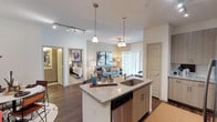 This thoughtfully designed one-bedroom, one-bathroom residence offers a seamless open-concept layout that connects the kitchen, dining, and living areas into a cohesive, functional living space. The kitchen serves as the heart of the home, featuring a granite-topped center island with an undermount sink, light wood cabinetry, subway tile backsplash, and a full suite of stainless steel appliances including a French door refrigerator, electric range, and built-in microwave. Track lighting overhead enhances the kitchen's contemporary aesthetic. A dedicated laundry closet with a stacked washer and dryer adds everyday convenience. The living room is bright and welcoming, with natural light streaming through sliding glass doors dressed in elegant floor-length drapes, complemented by rich hardwood-style flooring throughout. The bedroom is a tranquil retreat, offering generous natural light through large windows with stylish curtains, ceiling fan, and direct access to a spacious walk-in closet outfitted with multi-tier shelving and hanging rods. The bathroom is well-appointed with granite vanity countertops, dark wood cabinetry, and a full tub-and-shower combination with floor-to-ceiling tile surround.