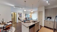 This thoughtfully designed one-bedroom, one-bathroom residence offers a seamless open-concept layout that connects the kitchen, dining, and living areas into a cohesive, functional living space. The kitchen serves as the heart of the home, featuring a granite-topped center island with an undermount sink, light wood cabinetry, subway tile backsplash, and a full suite of stainless steel appliances including a French door refrigerator, electric range, and built-in microwave. Track lighting overhead enhances the kitchen's contemporary aesthetic. A dedicated laundry closet with a stacked washer and dryer adds everyday convenience. The living room is bright and welcoming, with natural light streaming through sliding glass doors dressed in elegant floor-length drapes, complemented by rich hardwood-style flooring throughout. The bedroom is a tranquil retreat, offering generous natural light through large windows with stylish curtains, ceiling fan, and direct access to a spacious walk-in closet outfitted with multi-tier shelving and hanging rods. The bathroom is well-appointed with granite vanity countertops, dark wood cabinetry, and a full tub-and-shower combination with floor-to-ceiling tile surround.