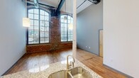 This 640 square foot loft apartment combines industrial aesthetics with modern amenities. The space boasts high ceilings with exposed ductwork and original brick walls, creating a unique urban ambiance. Large arched windows flood the open-concept living area with natural light, highlighting the rich hardwood floors. The kitchen features dark cabinetry, granite countertops, and stainless steel appliances. The bathroom offers a clean, contemporary design with a tub-shower combination and granite vanity. The 130 square foot bedroom provides a cozy retreat. Located in Charlotte, NC, this one-floor apartment effortlessly blends historic charm with contemporary living.