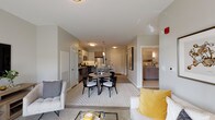 Located on Wareham Road in Plymouth, Massachusetts, this single-floor residence offers a thoughtfully designed open-concept layout with a neutral, contemporary aesthetic throughout. The living, dining, and kitchen areas flow seamlessly together, creating a cohesive and functional shared space. Light gray walls, plush carpeting in the living and sleeping areas, and light hardwood-style flooring in the kitchen contribute to a clean, modern atmosphere.

The kitchen is well-appointed with granite countertops, a mix of white upper cabinetry and wood-toned lower cabinets, a subway tile backsplash, and stainless steel appliances including a gas range, microwave, and refrigerator. A peninsula with seating provides additional prep space and a casual dining option alongside a dedicated dining area.

The bedrooms are comfortably sized, with one featuring large windows that bring in generous natural light and views of the surrounding grounds. A spacious walk-in closet with wire shelving provides ample storage. The bathroom includes a granite-topped vanity with gray cabinetry, tile flooring, and well-placed lighting. The living area opens via sliding glass doors to an outdoor patio with views of the landscaped community grounds.