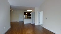 This single-floor space offers a thoughtfully designed open-concept layout that seamlessly connects the living area to the kitchen, creating a spacious and functional environment. Rich hardwood flooring extends throughout the main living area, adding warmth and a sense of continuity to the space.

The kitchen serves as a central focal point, featuring a raised breakfast bar with granite countertops that provides both workspace and casual seating. Dark cabinetry lines the kitchen, complemented by stainless steel appliances, including a full-size refrigerator, and a mounted microwave. Pendant lighting fixtures hang above the bar area, offering both task lighting and an element of style, while a fluorescent overhead fixture ensures ample illumination throughout the kitchen.

The open living area is framed by clean white walls, providing a neutral and versatile backdrop. Multiple doorways lead to additional rooms, suggesting a well-organized floor plan with private spaces accessible from the main living area. The doors feature classic panel detailing, contributing to a timeless aesthetic. The overall ambiance is bright and inviting, with a clean, modern sensibility that makes the space practical and comfortable for everyday living.