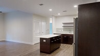 Located at The Pearl in Tampa, FL, this thoughtfully designed 2-bedroom, 2-bathroom residence offers a well-appointed single-floor layout with modern finishes throughout. The open-concept kitchen and living area serves as the heart of the home, featuring rich dark espresso cabinetry, gleaming white quartz countertops, a subway-tile backsplash, and a central island ideal for dining or entertaining. Stainless steel appliances — including a refrigerator, range, microwave, and dishwasher — complete the kitchen, which is further accented by floating shelves and recessed lighting. Wood-style plank flooring runs throughout the living spaces, adding warmth and continuity. The living room benefits from natural light through a set of glass French doors that open to an outdoor area, complemented by a ceiling fan overhead. Both bedrooms are generously sized with neutral tones and wood-style flooring, with one bedroom offering a window with lush outdoor views. Each bedroom is served by its own closet featuring wire shelving systems for organized storage. The bathrooms are finished with dark vanity cabinetry, granite countertops, and glass-enclosed walk-in showers with tile flooring, lending a clean, contemporary feel to the entire residence.