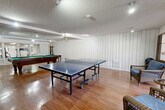 Located at 23825 Anza Ave in Torrance, CA, this single-floor recreational space is designed to serve as a dedicated game and activity room. The open layout provides ample room to accommodate multiple leisure activities simultaneously without feeling cramped. Warm hardwood flooring runs throughout, adding a classic, polished look to the space.

The main area is anchored by a full-size pool table with a green felt surface, complemented by a regulation ping-pong table, making the room well-suited for entertaining and active recreation. Wicker seating is positioned near the windowed entry, offering a comfortable area to relax between games. A wooden bookcase with display items adds a decorative touch along one of the white vertical-paneled walls.

Track lighting and recessed ceiling fixtures illuminate the space evenly across its textured popcorn ceiling, ensuring the room is well-lit for all activities. A dedicated fitness alcove, visible through a windowed partition, houses exercise equipment including a treadmill and elliptical machine, adding a functional wellness component to the space.

Natural light filters in through windows and a glass-paneled door, brightening the interior and providing a connection to the outdoors. The overall design is practical and activity-focused, offering a well-rounded environment for recreation and fitness.
