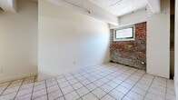 Located at 1418 W Marshall St in Richmond, VA, this one-bedroom, two-bathroom unit offers a compact and functional single-floor layout. A defining architectural feature throughout the space is the exposed red brick masonry, visible in the hallways, living area, and bedroom, lending a distinctive historic character to the interior. Light-toned ceramic tile flooring runs consistently throughout all rooms, creating a cohesive and easy-to-maintain surface.

The galley-style kitchen is well-equipped, featuring a double-basin stainless steel sink, teal-toned laminate countertops, white cabinetry, and a full suite of appliances including an electric range, over-the-range microwave, dishwasher, and refrigerator. An overhead fluorescent light fixture provides ample task lighting, and an electrical panel is conveniently accessible within the kitchen.

The bedroom offers a cozy footprint with a window that brings in natural light, complemented by exposed brick accent walls and painted ceiling beams that add to the unit's character. Three closets distributed throughout the unit provide practical storage solutions.

Both bathrooms feature tile flooring and clean white fixtures. The full bath includes a tub-shower combination, toilet, and vanity. Two hallways connect the various rooms, supporting a logical and navigable floor plan throughout this charming Richmond residence.