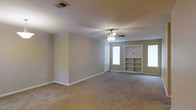 This single-floor space offers a clean and functional layout designed for comfortable everyday living. The main living area is generously sized, featuring wall-to-wall carpeting that adds warmth underfoot. Neutral-toned walls provide a versatile backdrop, making the space easy to personalize with a variety of décor styles.

A ceiling fan with an integrated light fixture is centrally positioned, offering both ambient lighting and air circulation throughout the room. Natural light filters in through multiple windows, lending the space a bright and airy feel. A full-length door provides access to an adjacent area or exterior, further enhancing the flow of the floor plan.

One of the standout features of the living area is the built-in shelving unit, which offers dedicated display and storage space, adding both practicality and architectural character to the room. The shelving is neatly integrated into the wall, creating a cohesive and polished look.

White trim and baseboards throughout provide clean contrast against the neutral walls, contributing to a tidy and well-maintained aesthetic. The overall ambiance is calm and inviting, with a straightforward, open design that offers flexibility for a range of furnishing arrangements and uses.