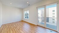 Located at 2922 W Marshall St in Richmond, VA, this thoughtfully designed one-bedroom, one-bathroom residence offers a clean, modern aesthetic throughout. The open-concept living and kitchen area is anchored by warm hardwood-style flooring and crisp white walls, creating a bright and airy atmosphere. The contemporary kitchen features stainless steel appliances, including a refrigerator, dishwasher, and range, complemented by white cabinetry with open shelving and dark accent storage towers that add a striking contrast. Recessed lighting illuminates the space efficiently. The bedroom is a comfortable retreat, featuring the same hardwood-style flooring, a ceiling fan, and a bold dark-wood built-in wardrobe that provides ample storage. A window and private balcony access fill the room with natural light and offer outdoor views of the surrounding neighborhood. The full bathroom is finished in a clean, contemporary style with light grey tile flooring, a quartz-topped vanity with a wood cabinet, and a full tub-shower combination. A hallway connects the living areas seamlessly. This residence combines functional design with modern finishes, making it a well-appointed home in the heart of Richmond.