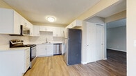 This two-floor residence offers a clean, contemporary interior with a neutral color palette and a cohesive design throughout. The kitchen is a functional centerpiece, featuring white shaker-style cabinetry, light countertops, and a full suite of stainless steel appliances including a gas range, built-in microwave, dishwasher, and a full-size refrigerator. Light-toned hardwood-style flooring runs through the kitchen and flows into the adjacent living areas, adding warmth and visual continuity.

The main level includes a spacious living area with textured ceilings, neutral walls, and natural light provided by a window with blinds. A staircase leads to the upper level, where the carpeted bedrooms offer a comfortable and quiet retreat. Each bedroom is generously sized, benefits from natural light through windows with blinds, and includes a closet with built-in railing for storage. The full bathroom is finished in white, featuring a tub-shower combination, a single-sink vanity with white cabinetry, and hardwood-style flooring. Clean lines and consistent finishes give the space a well-maintained, move-in-ready feel throughout both floors.