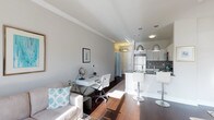 Unit 202 at 333 Central Avenue is a thoughtfully designed single-floor residence that maximizes its open-concept layout with clean lines and a bright, contemporary aesthetic. The living area is bathed in natural light, highlighting the rich dark hardwood flooring that flows seamlessly throughout the space. Crisp white walls and crown molding lend the interior a polished, refined character.

The kitchen is a standout feature, outfitted with white cabinetry, a decorative tile backsplash, stainless steel appliances, and a sleek white breakfast bar with modern bar seating — ideal for casual dining and entertaining. Pendant lighting in brushed metal tones hangs above the bar, adding a stylish focal point.

Adjacent to the kitchen, the open living space accommodates both a comfortable lounge area and a dedicated workspace, demonstrating the unit's versatility. The living area features a light-toned sofa with accent pillows, contributing to the overall airy and inviting atmosphere.

Natural light plays a key role throughout, amplifying the sense of openness and enhancing the neutral color palette of whites and soft grays. The thoughtful combination of functional design and modern finishes makes this unit a well-appointed and practical residence in a desirable location.
