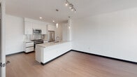 Located at 11036 Moorpark St in the North Hollywood neighborhood of Los Angeles, this single-floor unit showcases a clean, modern design with a cohesive aesthetic carried throughout every room. The open-concept living and kitchen area is bright and airy, with light hardwood-style flooring, crisp white walls, and large sliding glass doors that flood the space with natural light and provide access to an outdoor balcony with tree-lined views. The kitchen is outfitted with high-gloss white cabinetry, stainless steel appliances including a gas range, built-in microwave, refrigerator, and dishwasher, complemented by a peninsula with an integrated sink and light stone countertops — ideal for both cooking and casual dining. Pendant and track lighting add a refined touch overhead. The bedroom continues the modern theme with the same wood-style flooring, large sliding glass doors opening to a private balcony, and ample wall space. The hallway connects the living areas to the bedrooms and bathrooms with a smooth, logical flow. Bathrooms are finished with clean white surfaces, chrome fixtures, and a soaking tub-shower combination featuring elegantly tiled surround walls with a built-in niche. The overall ambiance is contemporary, minimal, and move-in ready.