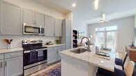 This thoughtfully designed single-floor residence offers a seamless blend of modern aesthetics and functional living. The open-concept kitchen is a standout feature, boasting granite countertops, a large center island with a built-in sink and bar seating, gray shaker-style cabinetry, a herringbone tile backsplash, and a full suite of stainless steel appliances including a french door refrigerator, electric range, and over-the-range microwave. Pendant lighting accents the island, while light wood-style flooring flows throughout the main living areas. The living room is bright and inviting, featuring elevated ceilings, a ceiling fan, and a glass-panel door that fills the space with natural light. The bedroom offers plush carpeting, large windows with ample natural light, and direct access to a walk-in closet with built-in rod storage. The bathroom is elegantly appointed with a wide double vanity topped with granite countertops, gray cabinetry with brushed hardware, a large frameless mirror, and open built-in shelving for organized storage. Throughout the residence, a clean, neutral palette and contemporary finishes create a cohesive and welcoming atmosphere.
