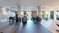 Located at 80 Batterson Park Rd in Farmington, CT, this expansive fitness center offers a comprehensively equipped exercise facility across a single, generously sized floor. The space is thoughtfully divided into distinct workout zones, each designed to support a full range of fitness activities.

The strength training area features a robust selection of equipment, including a multi-station cable machine, free weights, dumbbells, and adjustable benches, all set on durable rubber flooring. Exposed brick accent walls and large windows allow natural light to pour in, creating an energizing atmosphere. Structural columns with two-tone detailing add an architectural rhythm throughout the space.

The cardio zone is lined with treadmills and stair climbers, complemented by bold, sports-themed wall murals featuring motivational athlete quotes that reinforce an active mindset. A separate room with sleek black-framed glass partition doors houses recumbent bikes and cycling equipment, with wall-mounted screens for interactive workouts and a yoga/exercise mat for stretching.

Linear LED lighting runs across the ceilings throughout, providing bright, even illumination. The combination of hard flooring and rubber mat surfaces accommodates diverse workout styles. The overall design strikes a balance between modern aesthetics and functional performance, making this fitness center a well-appointed destination for serious training.