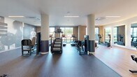 Located at 80 Batterson Park Rd in Farmington, CT, this expansive fitness center offers a comprehensively equipped exercise facility across a single, generously sized floor. The space is thoughtfully divided into distinct workout zones, each designed to support a full range of fitness activities.

The strength training area features a robust selection of equipment, including a multi-station cable machine, free weights, dumbbells, and adjustable benches, all set on durable rubber flooring. Exposed brick accent walls and large windows allow natural light to pour in, creating an energizing atmosphere. Structural columns with two-tone detailing add an architectural rhythm throughout the space.

The cardio zone is lined with treadmills and stair climbers, complemented by bold, sports-themed wall murals featuring motivational athlete quotes that reinforce an active mindset. A separate room with sleek black-framed glass partition doors houses recumbent bikes and cycling equipment, with wall-mounted screens for interactive workouts and a yoga/exercise mat for stretching.

Linear LED lighting runs across the ceilings throughout, providing bright, even illumination. The combination of hard flooring and rubber mat surfaces accommodates diverse workout styles. The overall design strikes a balance between modern aesthetics and functional performance, making this fitness center a well-appointed destination for serious training.