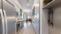 Located at 1010 Singleton Blvd in Dallas, TX, this well-appointed one-bedroom, one-bathroom residence demonstrates how smart design can maximize every square foot. The galley-style kitchen is a standout feature, lined on both sides with gray shaker cabinetry accented by matte black hardware, open shelving, and white quartz countertops. Stainless steel appliances — including a range, microwave, and dishwasher — complement the classic subway tile backsplash, while light wood-tone flooring runs seamlessly throughout the space. Opposite the kitchen, a built-in storage and workspace area provides ample organization solutions. The generously sized bedroom offers a serene retreat, featuring direct access to a private outdoor area through large glass doors that invite natural light and outdoor views. A ceiling fan, elegant chandelier, and curated wall space contribute to the room's warm, livable ambiance. The full bathroom is cleanly finished with large-format floor tile, a white vanity with quartz countertop, a full mirror, and a tub-shower combination with white tile surround. Throughout the residence, the consistent use of neutral tones, modern fixtures, and efficient built-in storage creates a cohesive, functional living environment.