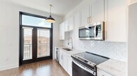 Located at 601 Indian St in the heart of Savannah, Georgia, this efficiently designed single-floor unit offers a thoughtfully arranged layout that maximizes every square foot. The kitchen serves as a centerpiece of the space, showcasing crisp white shaker cabinetry with brushed nickel hardware, a herringbone-patterned tile backsplash, stainless steel appliances including a range, microwave, dishwasher, and refrigerator, and a undermount sink beneath a modern pendant light. Black-framed French doors open to a private balcony, flooding the kitchen with natural light and offering views of the surrounding Savannah streetscape. Wide-plank hardwood-style flooring runs throughout, providing warmth and continuity. The main living area features striking black-framed arched windows that frame outdoor views while bathing the room in daylight. The bathroom is clean and contemporary, finished with wood-look flooring, a glass-enclosed shower, and a crisp white palette. Additional functionality is provided through a dedicated laundry area and utility room. A bold, dark three-panel entry door adds a sophisticated design accent. This unit blends modern finishes with classic Savannah character for a polished, move-in-ready space.