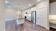 Located at 1980 Icon Way in Knoxville, Tennessee, this well-appointed 2-bedroom, 2-bathroom single-story residence offers a thoughtfully designed layout with modern finishes throughout. The open-concept kitchen and living area serves as the heart of the home, featuring crisp white shaker cabinetry, a white subway tile backsplash, quartz countertops, and stainless steel appliances including a range, microwave, and refrigerator. A central island with a built-in sink and pendant lighting above adds both functionality and style, while recessed lighting brightens the entire space. Rich hardwood-style flooring flows seamlessly throughout the home, complementing the neutral warm-gray wall tones. A hallway connects the main living area to both bedrooms, each of which benefits from natural light through window blinds and direct access to a dedicated walk-in closet outfitted with multi-tier wire shelving systems. The primary bedroom is generously proportioned and includes a ceiling fan. Both bathrooms are well-finished; one features a tub-shower combination with gray subway tile surround and matte black fixtures paired with a white vanity. The overall ambiance is clean, contemporary, and move-in ready.