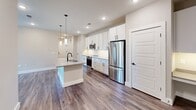 Located at 1980 Icon Way in Knoxville, Tennessee, this well-appointed 2-bedroom, 2-bathroom single-story residence offers a thoughtfully designed layout with modern finishes throughout. The open-concept kitchen and living area serves as the heart of the home, featuring crisp white shaker cabinetry, a white subway tile backsplash, quartz countertops, and stainless steel appliances including a range, microwave, and refrigerator. A central island with a built-in sink and pendant lighting above adds both functionality and style, while recessed lighting brightens the entire space. Rich hardwood-style flooring flows seamlessly throughout the home, complementing the neutral warm-gray wall tones. A hallway connects the main living area to both bedrooms, each of which benefits from natural light through window blinds and direct access to a dedicated walk-in closet outfitted with multi-tier wire shelving systems. The primary bedroom is generously proportioned and includes a ceiling fan. Both bathrooms are well-finished; one features a tub-shower combination with gray subway tile surround and matte black fixtures paired with a white vanity. The overall ambiance is clean, contemporary, and move-in ready.
