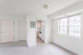 This single-floor unit is laid out with a practical, straightforward floor plan visible across several interconnected rooms. The living area is generously proportioned, finished with neutral gray carpet and cream-toned walls that create a clean, understated atmosphere. A double closet and an additional door provide convenient storage and access directly from this space. Natural light enters through gridded double-hung windows, lending the room a bright, open feel.

The separate kitchen is compact yet fully functional, featuring light blush-toned cabinetry, white countertops, and tile flooring in warm earth tones. It is equipped with an electric range, a dishwasher, a refrigerator, and a sink positioned beneath a window. The layout makes efficient use of the available space.

The bedroom areas are carpeted and well-lit, each with windows that invite natural light. One bedroom benefits from corner windows on two walls, providing an especially airy quality. Closet access is available within the sleeping areas.

The bathroom features a classic black-and-white tile design, with white square wall tiles framed by a bold black border, giving it a timeless, retro aesthetic. An electrical panel is accessible within the unit. Overall, the space presents a neutral, move-in-ready environment with consistent finishes throughout.