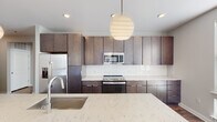 Located at 539 Foster St in Durham, NC, this single-floor unit showcases a cohesive modern design with warm wood-look plank flooring running throughout the space. The open-concept kitchen serves as a central highlight, featuring floor-to-ceiling dark espresso cabinetry, a white subway tile backsplash, and a generous island topped with striking veined quartz countertops. A sculptural globe pendant light anchors the space above the island, while stainless steel appliances—including a French door refrigerator, range, and microwave—complete the contemporary aesthetic.

The living area is bright and open, benefiting from multiple windows fitted with horizontal blinds that allow natural light to filter in while framing views of the surrounding neighborhood. The neutral gray walls and clean white trim create a versatile backdrop throughout.

Two bathrooms serve the unit, each finished with dark wood-toned floating vanities and white countertops. The primary bathroom features a double-sink vanity with an expansive mirror and connects directly to a bedroom. A secondary bathroom includes a tall storage tower for added functionality. The hallways connect rooms efficiently, reinforcing the layout's practical and well-organized flow.