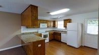 This two-floor home offers a practical and well-organized layout designed to maximize functionality. The kitchen serves as a notable focal point, showcasing warm-toned wood cabinetry that extends to the upper and lower walls, providing generous storage throughout. A peninsula with a laminate countertop extends into the space, offering additional prep area and a natural division between the kitchen and adjacent living areas. White appliances — including a refrigerator, electric range, built-in microwave, and dishwasher — are neatly integrated into the layout. A double basin sink is positioned beneath a window, allowing natural light to brighten the workspace. The floors throughout the kitchen are finished in light-toned hardwood, adding warmth to the room. A textured ceiling with a skylight-style fluorescent fixture provides even overhead lighting. The overall design reflects a classic, no-frills aesthetic with an emphasis on practicality. With two floors, the home offers a clear separation of living spaces, making it well-suited for a variety of occupants. The combination of wood accents, durable flooring, and ample cabinetry gives the home a timeless, functional character throughout.