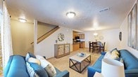 This two-story residence offers a practical and comfortable layout centered around an open-concept main level. The living room serves as the heart of the space, featuring carpet flooring, a textured ceiling, and room for ample seating. A wooden staircase with a warm oak railing rises along one wall, providing access to the upper floor while adding a structural focal point to the room.

The main level flows seamlessly into the kitchen and dining area. The kitchen is equipped with dark appliances, including a range and overhead microwave, set against warm wood cabinetry. Tile flooring transitions naturally from the kitchen into the adjacent dining area, which is illuminated by a decorative pendant light fixture and accommodates a full dining table and chair set.

The open sightlines between the living, dining, and kitchen areas create a cohesive and connected feel throughout the main level, making the space well-suited for everyday living and entertaining. Overhead lighting is present throughout, and HVAC vents are integrated into the ceiling. The upper floor provides additional living space accessible via the interior staircase.