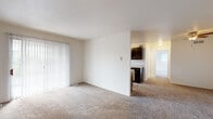 This single-story unit offers a practical and well-organized layout designed for comfortable everyday living. The living area is generously sized, featuring neutral wall-to-wall carpet and a large sliding glass door fitted with vertical blinds that invite abundant natural light into the space. The open sightlines connect the living area to the kitchen and a carpeted hallway leading to the private rooms.

The galley-style kitchen is efficiently laid out with dark cabinetry lining both walls, providing ample storage space. It is equipped with stainless steel appliances, including a gas range, refrigerator, built-in microwave, and dishwasher, complemented by light countertops and a single-basin sink. Light wood-look flooring runs throughout the kitchen, adding a clean, modern contrast to the dark cabinetry.

The bedroom is well-proportioned with soft carpeting, two windows that provide cross-ventilation and natural light, and a wide louvered bi-fold closet offering generous storage capacity. A ceiling fan adds to the room's comfort.

The bathroom features wood-look tile flooring, a dark vanity with a light countertop, and a full tub and shower combination positioned beneath a window with vertical blinds. The overall aesthetic throughout the space is clean, neutral, and move-in ready.
