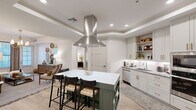 Located at 98 South River Drive in Tempe, Arizona, this thoughtfully designed 2-bedroom, 2-bathroom residence offers a cohesive blend of modern finishes and functional living across a single floor. The kitchen serves as a standout centerpiece, featuring soft sage-green cabinetry accented with brushed gold hardware, granite countertops, a white subway tile backsplash, stainless steel appliances, and a large island with seating — all complemented by a striking stainless steel range hood overhead. Light wood-look flooring flows throughout, tying the spaces together seamlessly. The living room offers natural light through dual windows, enhanced by a statement brass chandelier and tray ceiling detailing. The primary bedroom is generously sized, offering a ceiling fan and window, while its walk-in closet provides dual hanging rods and built-in shelving for ample storage. The second bedroom is equally comfortable with its own closet. Both bathrooms feature granite vanity tops, deep green cabinetry with gold hardware, subway tile surrounds, and soaking tub-shower combinations. Each closet is well-organized with built-in shelving systems. The overall ambiance is modern yet warm, with refined design details carried consistently throughout the home.