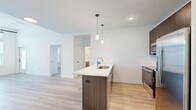 Located at 8550 N Main St in Kansas City, MO, this well-appointed 3-bedroom, 2-bathroom unit offers a thoughtfully designed single-level layout. The open-concept kitchen and living area serves as the heart of the home, featuring a large island with a white quartz countertop, dark wood cabinetry, white subway tile backsplash, and a full suite of stainless steel appliances, including a refrigerator, range, and built-in microwave. Stylish pendant lighting and light wood-look flooring complete the modern aesthetic. The living room is bright and airy, with expansive windows that invite abundant natural light and offer outdoor views, complemented by high ceilings and a ceiling fan. A private balcony is accessible directly from the living area. The three bedrooms are carpeted for comfort, each featuring ceiling fans and dedicated closet space. The spacious primary bedroom includes its own closet access. Both bathrooms are finished with light tile flooring, walnut-toned vanities, white quartz countertops, and black hardware accents. One bathroom features a walk-in shower, while the other offers a full tub-shower combination. Clean white walls and crisp panel doors throughout lend the entire space a fresh, contemporary feel.