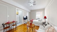 Located at 2505 13th St NW in Washington, DC's vibrant Columbia Heights neighborhood, this efficient one-bedroom, one-bathroom unit offers a thoughtfully organized layout across a single floor. The spacious main room serves as the primary living and sleeping area, showcasing warm hardwood floors, classic wainscoting-style wall trim, and a ceiling fan with integrated lighting. Natural light fills the room through a large double-hung window, creating a bright and welcoming ambiance. The room comfortably accommodates a full-sized bed, seating area, and a dedicated workspace. A separate kitchen is accessed through a doorway and features warm wood cabinetry, granite-style countertops, a gas range, refrigerator, and a stainless steel sink — everything needed for everyday cooking. The bathroom is clean and simply appointed, with a white vanity, medicine cabinet mirror, and a shower-tub combination with tiled surroundings. A closet provides additional storage. The unit's neutral gray walls, classic architectural detailing, and hardwood flooring throughout give it a timeless character well-suited to urban living in one of DC's most walkable and dynamic neighborhoods.