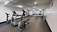 This fitness center offers a comprehensive workout environment designed to support a wide range of exercise routines. The space is outfitted with multiple cardio machines, including treadmills and elliptical trainers, positioned for ease of use and accessibility. A multi-station cable weight machine anchors the strength training area, providing options for a variety of resistance exercises. Stability and exercise balls are also available, adding versatility for core and flexibility training. The flooring throughout is a durable rubber surface, providing excellent traction and cushioning suited for high-impact activity. A large wall-to-wall mirror runs along one side of the room, visually expanding the space while allowing users to monitor their form during workouts. Recessed lighting in the textured ceiling ensures the area is well-lit, contributing to a clean and functional atmosphere. The layout is thoughtfully organized to maximize usable floor space while keeping equipment accessible. Overall, the fitness center presents a practical and well-maintained environment suitable for a broad range of fitness goals.