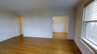 This single-floor space showcases a timeless and understated aesthetic, defined by warm hardwood floors that run throughout, lending a sense of continuity and natural warmth. The interior is finished in a crisp, neutral white palette across both the walls and ceiling, creating a bright and airy atmosphere that feels open and versatile.

Crown moulding trims the ceiling perimeter, adding a classic architectural detail that elevates the overall character of the space. White baseboards complement this finish, framing the floors and reinforcing the cohesive, traditional styling throughout.

The main room is generously proportioned, offering ample space for flexible furnishing arrangements. A doorway opens directly into an adjoining room, also finished in the same neutral tones and hardwood flooring, promoting a seamless flow between areas. This interconnected layout is well-suited for a variety of uses, from living and dining configurations to home office or multi-purpose arrangements.

Overall, the space presents a clean, move-in ready interior with classic finishes that provide a solid foundation for a range of interior design styles.