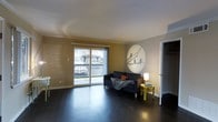 This single-floor residence offers a well-organized and inviting layout designed for comfortable everyday living. The living area serves as the heart of the space, featuring rich, dark hardwood flooring that runs throughout and provides a sleek, grounding contrast to the warm, neutral-toned walls. A large sliding glass door floods the room with natural light and opens directly onto a private balcony, offering views of the surrounding neighborhood and extending the sense of space beyond the interior.

The living room is enhanced by a distinctive circular wall mural depicting birds perched on a wire, adding an artistic and personal touch to the décor. Crown molding along the ceiling provides a refined architectural detail that elevates the overall finish of the room.

A closet situated near the living area offers practical storage solutions, contributing to the functional layout of the space. The room's clean lines and open floor plan allow for flexible furniture arrangement, making it adaptable to a variety of living styles. Overall, the space presents a bright, tidy, and welcoming atmosphere, combining thoughtful design details with everyday practicality in a compact, efficient single-level footprint.