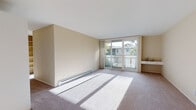 This single-floor residence offers a thoughtfully laid-out interior with a clean, neutral aesthetic throughout. The living area is generously proportioned, featuring plush wall-to-wall carpeting and large sliding glass doors that open to a private balcony, flooding the space with natural light and providing views of the surrounding neighborhood and mature palm trees. A built-in wall desk adds a practical touch to this main living space, which is also equipped with a baseboard heating system for year-round comfort.

The kitchen is efficiently designed with white cabinetry that extends to the ceiling for ample storage, light stone-toned countertops, a stainless steel sink, and white appliances including an electric range and overhead ventilation hood. The tile flooring adds durability and easy maintenance to this functional cooking space.

The bedroom is well-sized with soft carpeting and a wide bank of windows that frame views of palm trees and the surrounding landscape, ensuring excellent natural light. A ceiling fan with integrated lighting provides both airflow and illumination, and a closet offers convenient storage.

The bathroom is complete with a tub and shower combination fitted with sliding glass doors, a vanity with a large mirror, and tile flooring, presenting a clean and practical design. The overall ambiance of the residence is bright, neutral, and move-in ready.