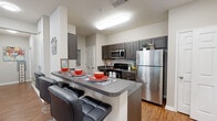 Located at 1410 Nottingham St in Huntsville, Texas, this single-floor residential unit offers a well-designed layout that balances comfort and functionality. The open-concept living room is bright and spacious, featuring wood-style flooring, a ceiling fan, large windows that invite natural light, and ample room for both lounging and entertaining. The kitchen is a standout feature, designed in a galley style with dark espresso cabinetry, granite-style countertops, stainless steel appliances including a refrigerator, microwave, and range, as well as a double sink and dishwasher. A breakfast bar with bar seating connects the kitchen to the living area, making it ideal for casual dining. A dedicated in-unit laundry area is conveniently accessible from the kitchen. The bedrooms offer comfortable, carpeted or wood-style flooring spaces with windows providing outdoor views and natural light, along with room for a desk setup suitable for studying or remote work. The bathrooms are functional and clean, each featuring a shower-tub combo with a curtain, vanity with storage, and wood-style flooring. Throughout the unit, the neutral color palette and consistent finishes create a cohesive, modern ambiance.