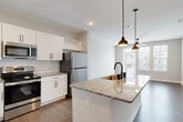 This single-floor residence is designed with a clean, contemporary aesthetic that emphasizes open living and functional design. The kitchen serves as the focal point, showcasing an expansive granite-topped island with an undermount sink and matte black faucet, illuminated by a pair of industrial-style pendant lights. White shaker cabinetry lines the walls above a classic subway tile backsplash, while stainless steel appliances — including a range, microwave, and refrigerator — provide a polished finish. Wood-look flooring runs throughout the main living areas, adding warmth to the neutral color palette. Built-in open shelving near the kitchen offers additional storage and display space.

The living area is bright and airy, benefiting from large windows with views of the surrounding neighborhood and access to a balcony. A ceiling fan adds comfort to the space. The bedroom is carpeted for coziness, fitted with a ceiling fan, and receives ample natural light through double windows. A generously sized walk-in closet with wire shelving provides versatile storage. The bathroom features a granite vanity countertop with an undermount sink and brushed nickel fixtures, maintaining the refined design language found throughout the residence.